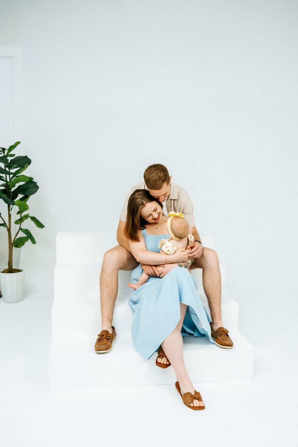 Happy young family with newborn baby sitting on white steps in a bright studio setting.