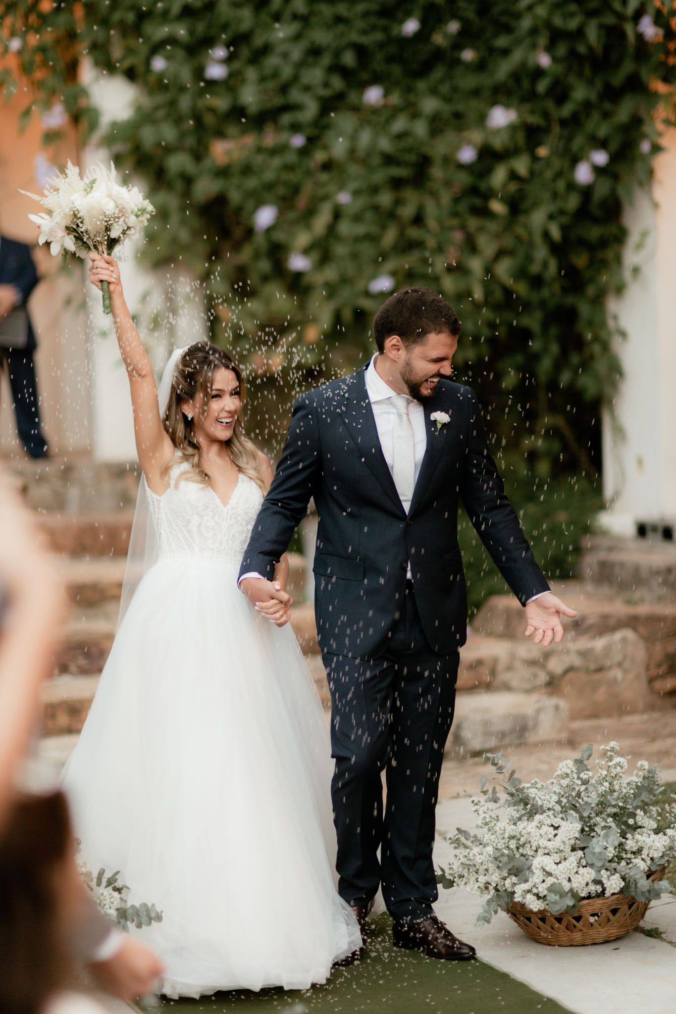 Newlyweds celebrate joyfully amid falling confetti in an outdoor garden ceremony.