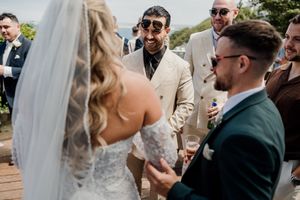 Bride and groom laughing with guests in sunglasses at an outdoor wedding reception celebration.