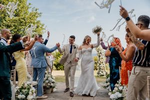 Bride and groom walk down the aisle as guests celebrate with confetti and ribbon wands at an outdoor wedding ceremony.