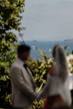 Blurred bride and groom holding hands with scenic ocean and island views in the background on their wedding day.