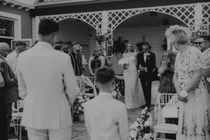 Black and white outdoor wedding ceremony with bride walking down the aisle surrounded by guests.