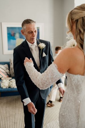 Emotional father sees bride daughter for first time in lace wedding gown during wedding day first look.