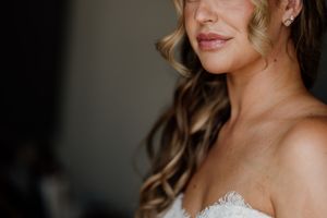 Close-up of a bride with soft curled hair, subtle makeup, pearl earrings, and a strapless lace wedding gown.