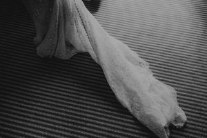 Black and white photo of a delicate lace wedding dress train draped on a textured floor.