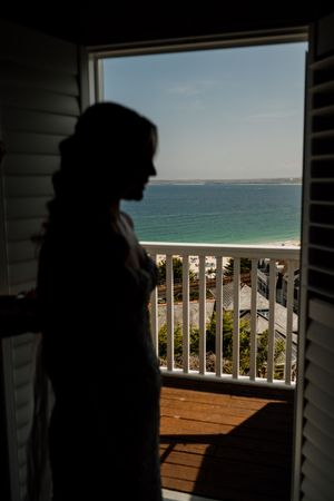 Silhouette of a person standing by an open door with a scenic ocean and beach view from a balcony.