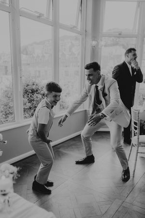 Black and white photo of a groom dancing with a young boy at a wedding reception in an elegant room.