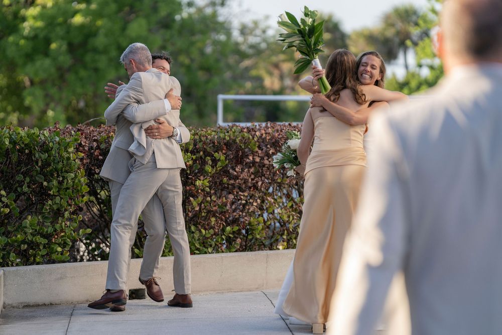 Wedding guests embracing outdoors, sharing joyful hugs in elegant neutral attire at a sunny garden celebration.