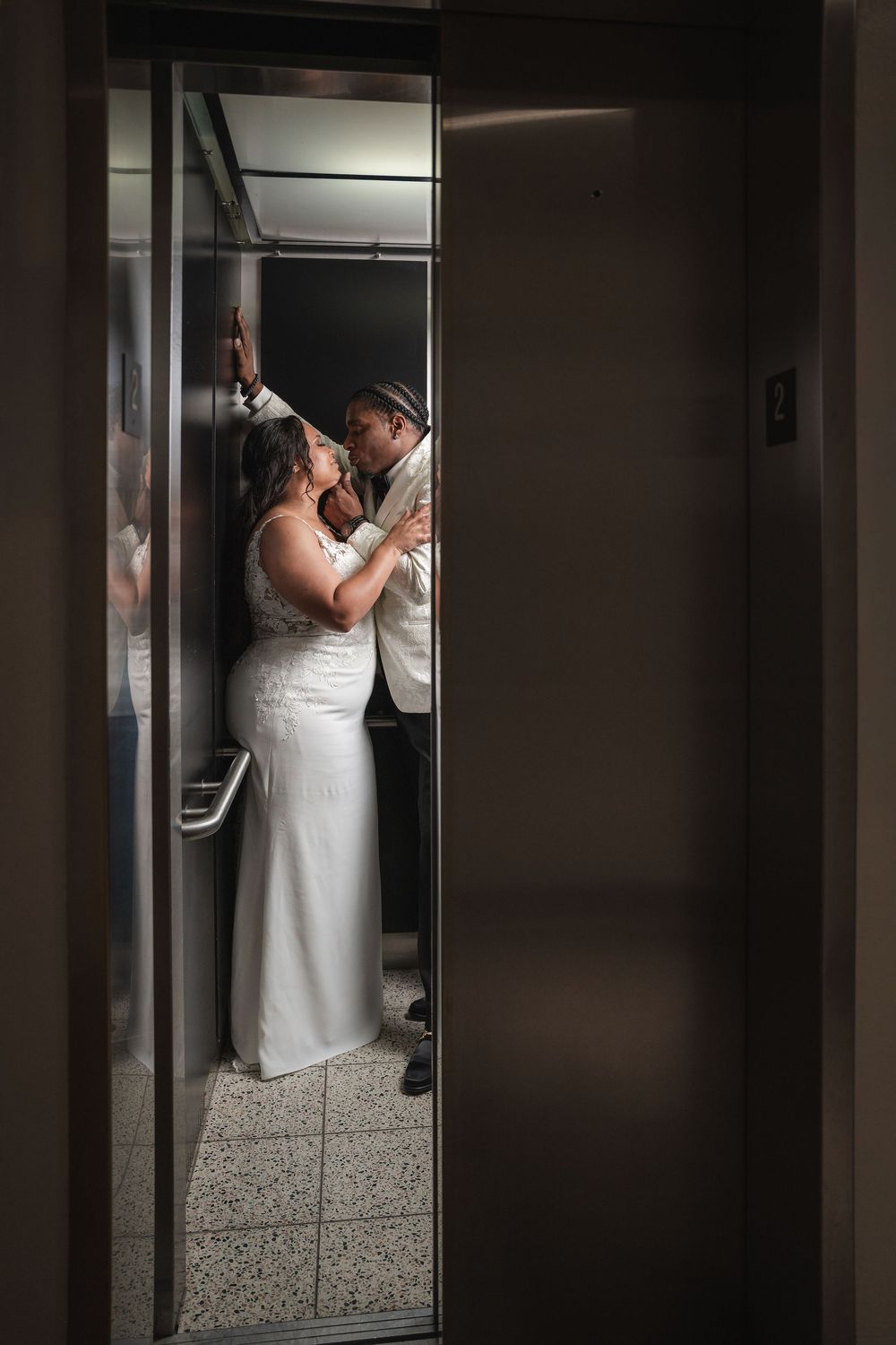 A bride and groom share an intimate moment in an elevator, the bride in a white gown and groom in a suit.