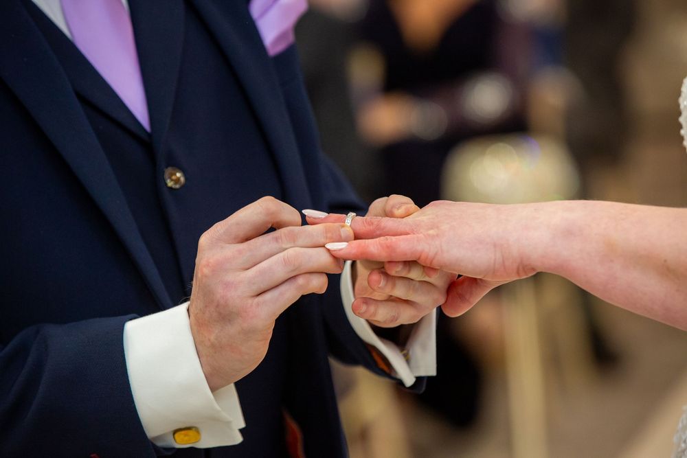 Groom placing a wedding ring on bride's finger during a wedding ceremony.