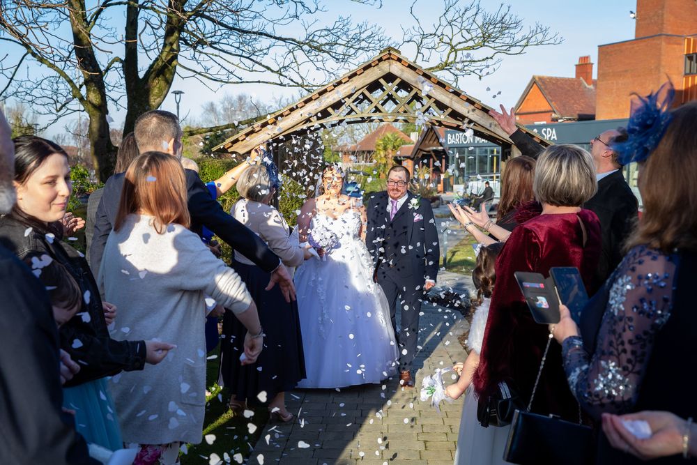 Bride and groom walk through confetti shower surrounded by guests at outdoor wedding ceremony.