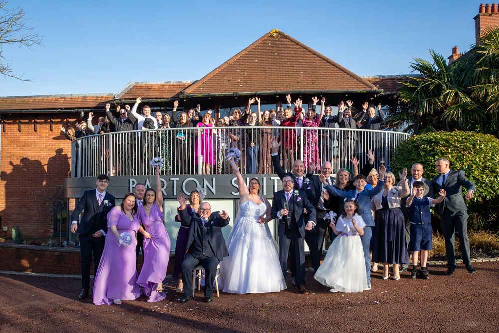 Wedding party celebrating outside Barton Suite venue, bride in white gown with guests in purple dresses and formal wear.