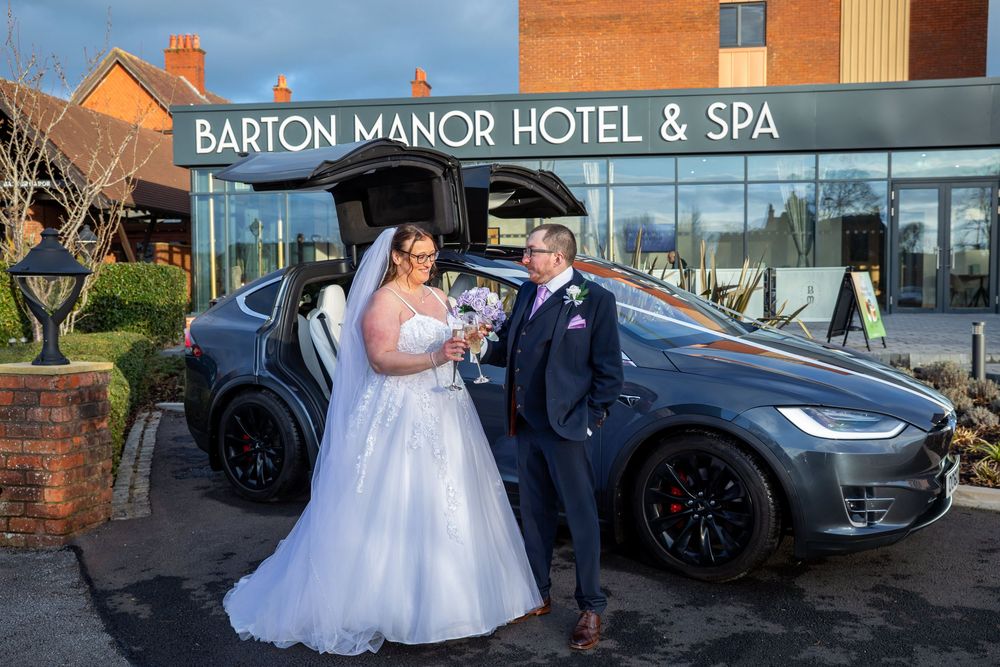 Bride and groom posing with a Tesla outside Barton Manor Hotel & Spa on their wedding day.