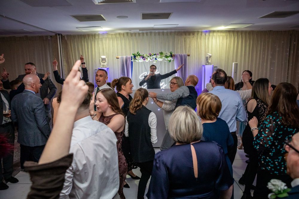 Guests dancing and celebrating at a lively wedding reception in a decorated banquet hall.