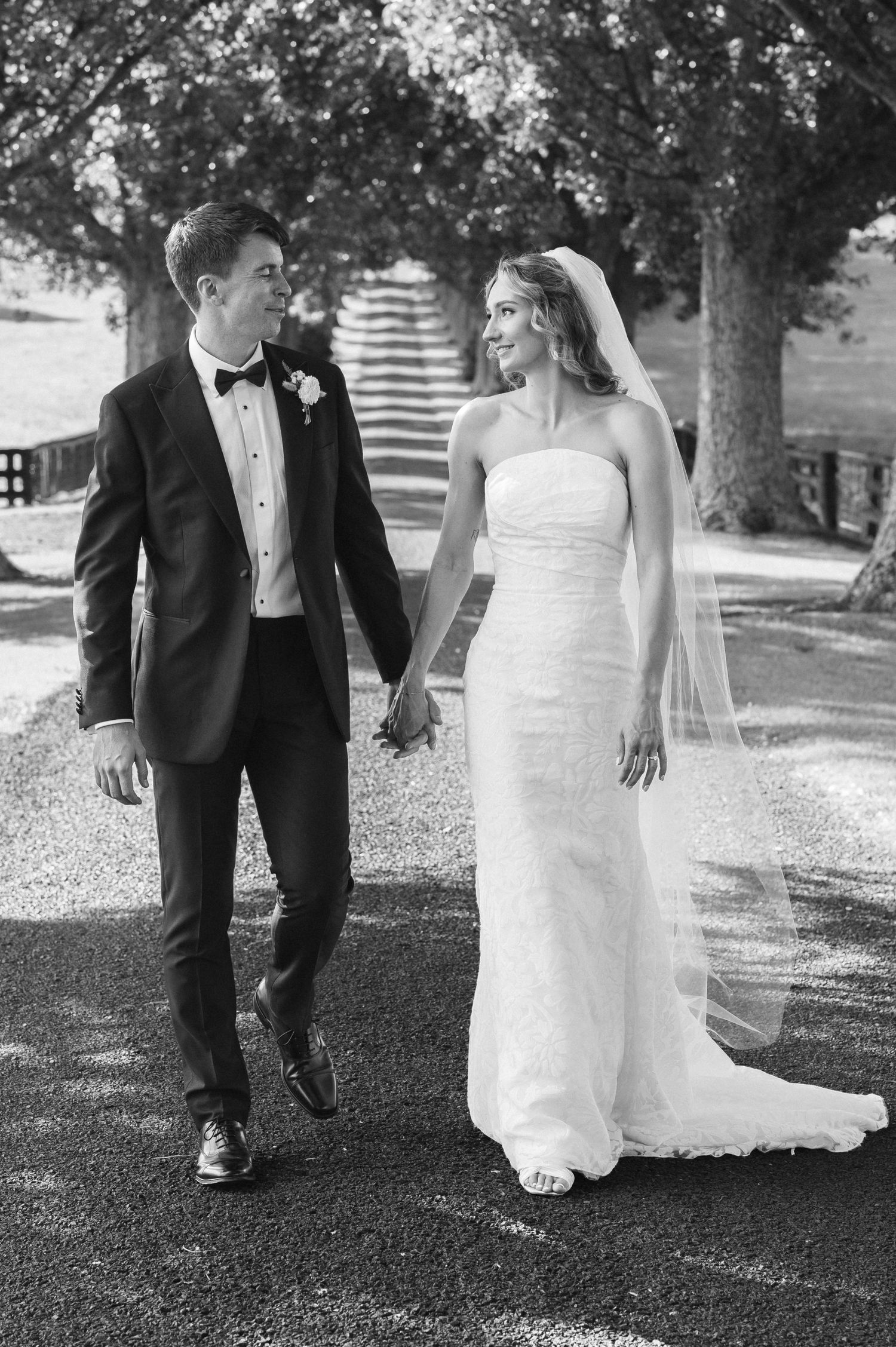 Black and white photo of a bride and groom holding hands, walking together outdoors on their wedding day.