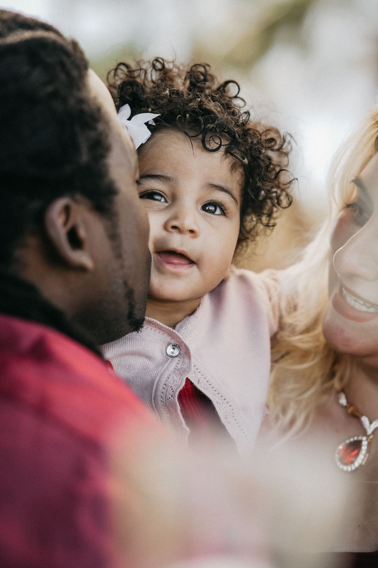 Close up portrait of a happy child with curly hair snuggling between parents in an intimate family moment.