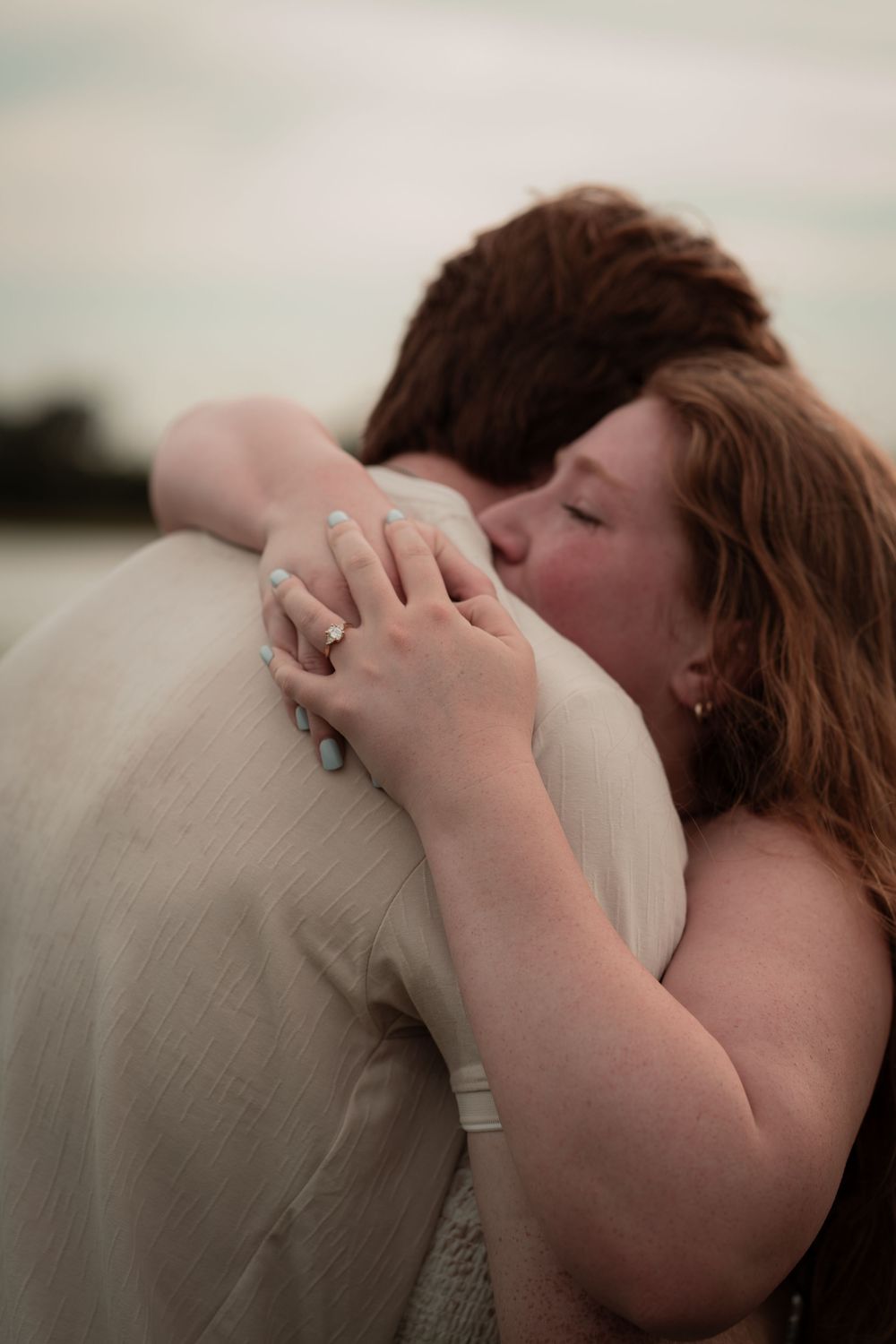 Couple sharing a romantic embrace outdoors, woman with red hair kissing man's cheek wearing wedding rings.