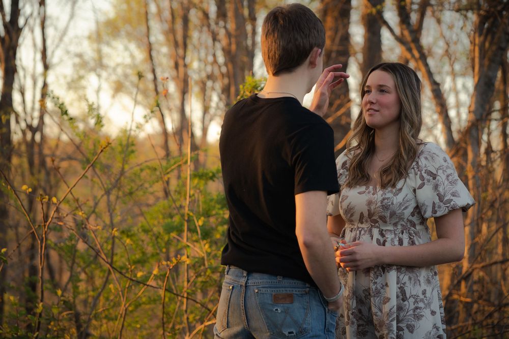A young couple shares a tender moment in a golden autumn forest, the man gently touching the woman's hair at sunset.