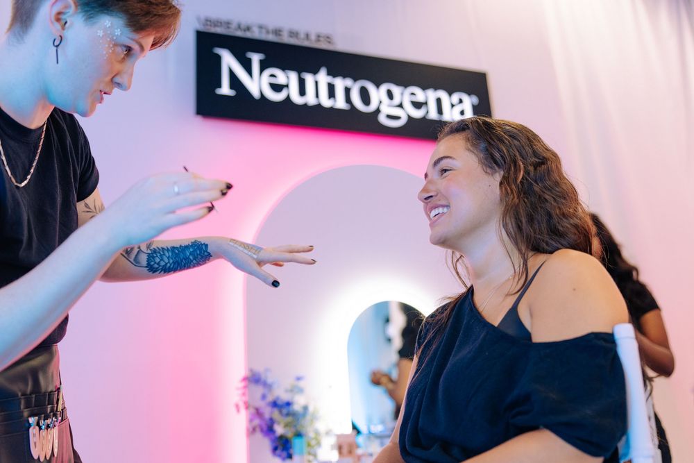 Woman smiling at a Neutrogena beauty event, receiving a hand consultation from a makeup artist.