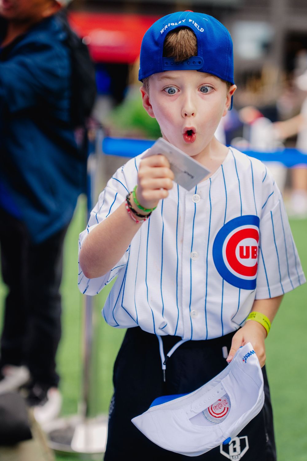 Young boy in Chicago Cubs jersey and cap pointing excitedly at Wrigley Field.