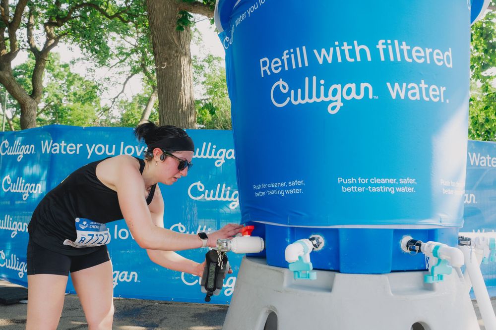Woman refilling water bottle at a Culligan filtered water station outdoors at a sunny event.