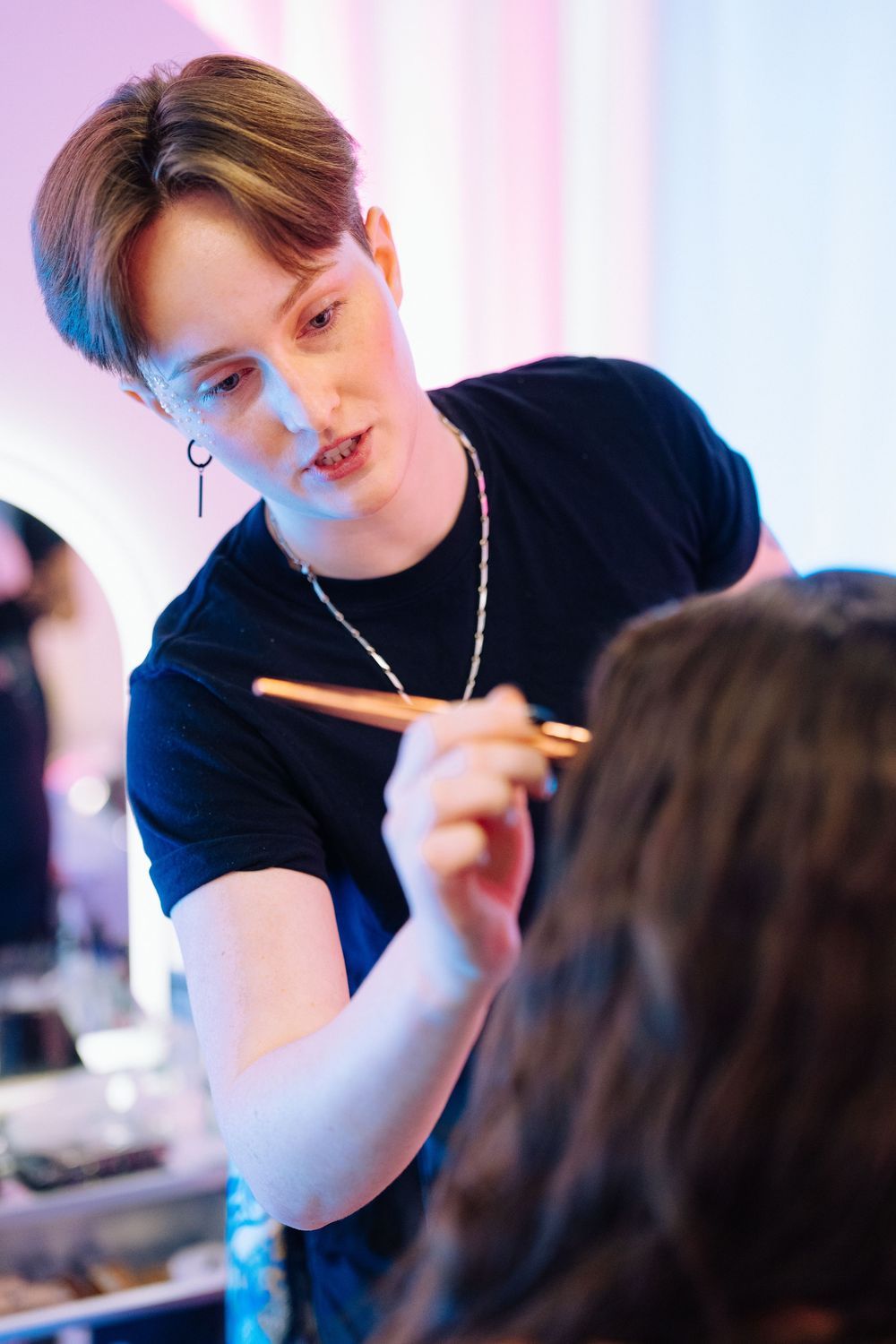 Professional makeup artist applying makeup with a brush on a client in a bright studio setting.