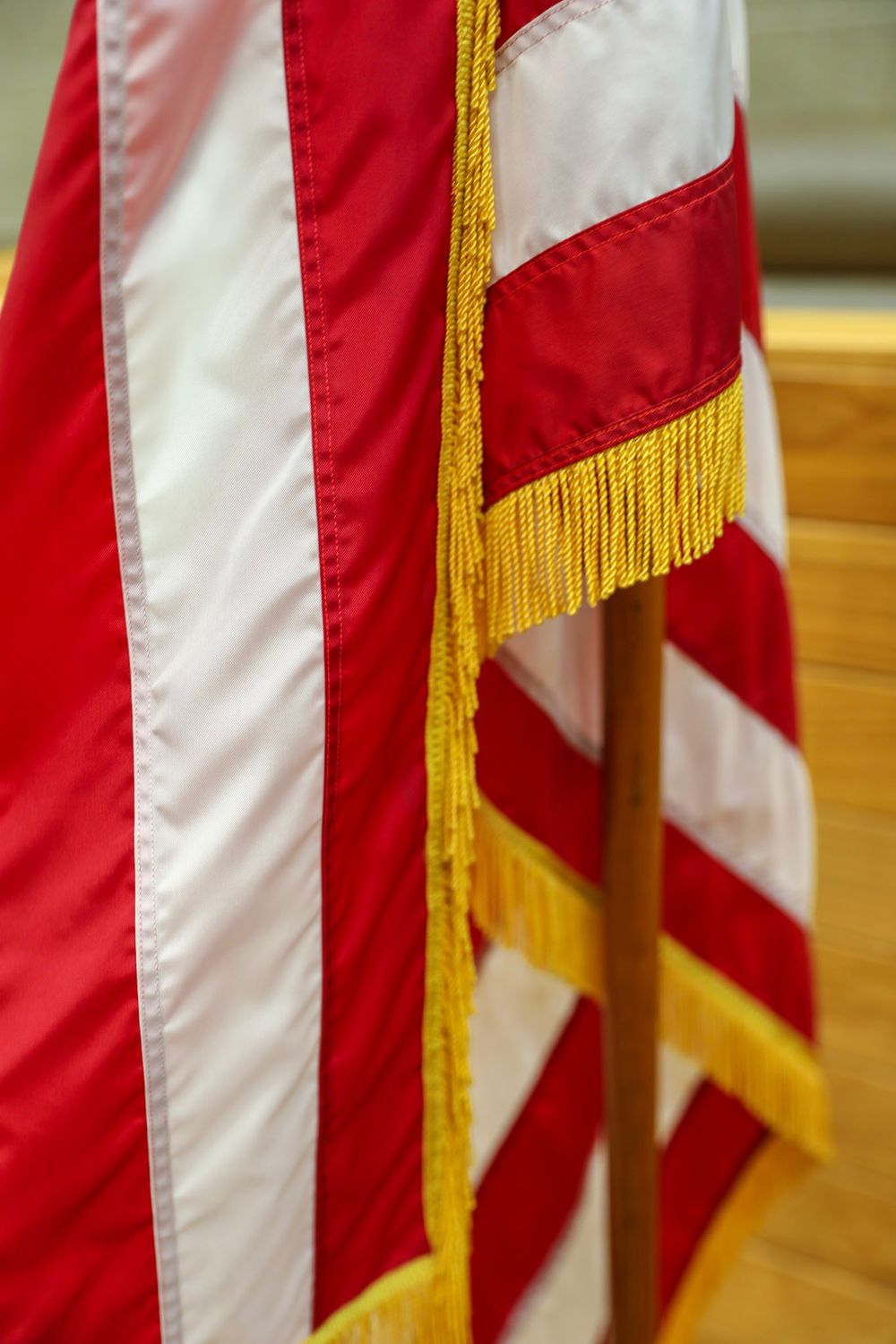 Close-up of an American flag with gold fringe displayed indoors next to a wooden podium.