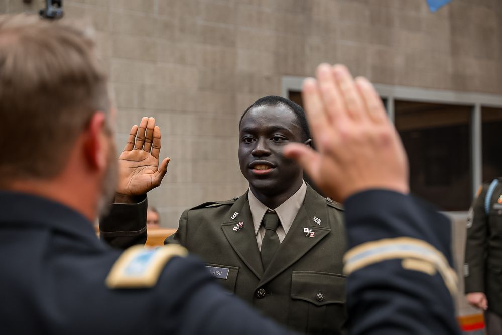 Military officer taking an oath ceremony, raising right hand in formal uniform indoors.