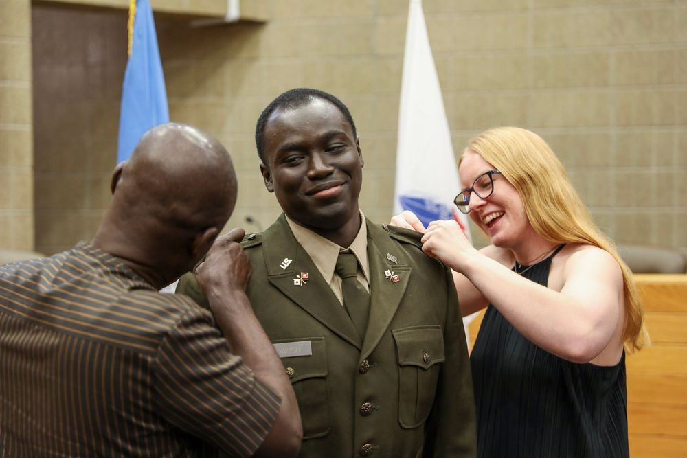 Military officer in uniform smiles as two people pin insignia on his shoulders during a promotion ceremony.