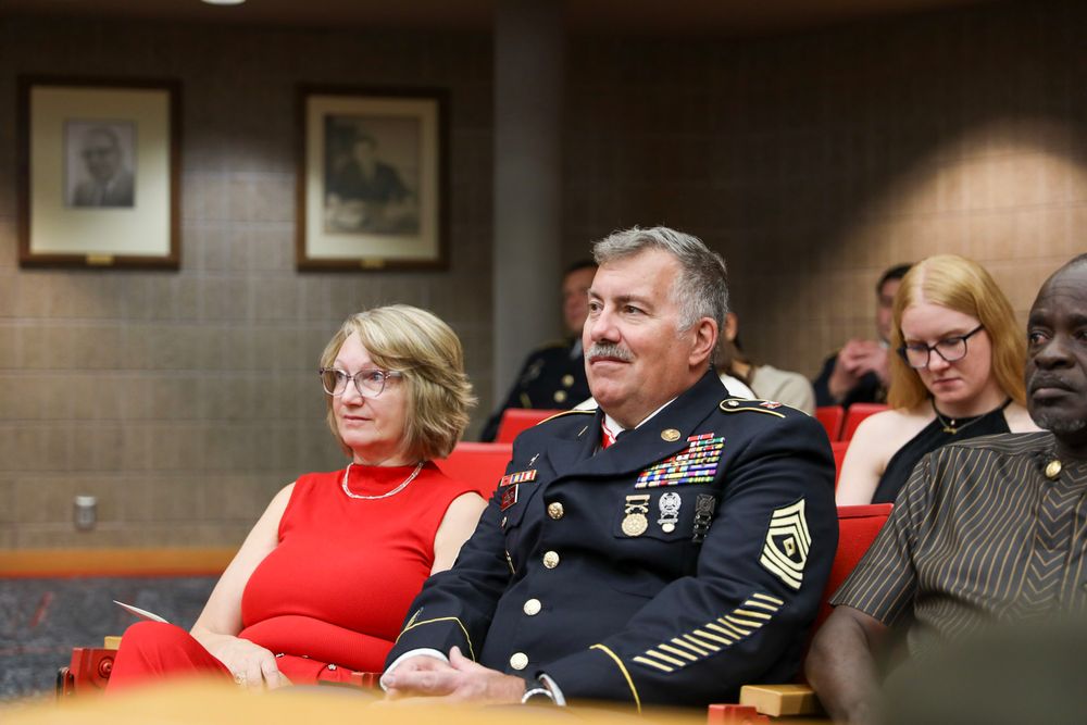 Military officer in dress uniform seated with civilians at a formal indoor event.