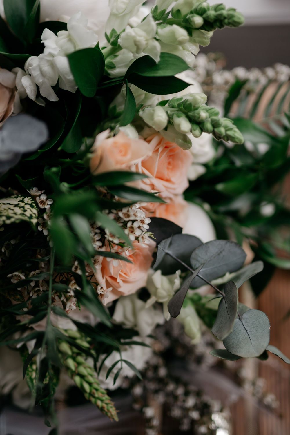 Elegant wedding bouquet with peach roses, white flowers, and eucalyptus greenery in soft focus.