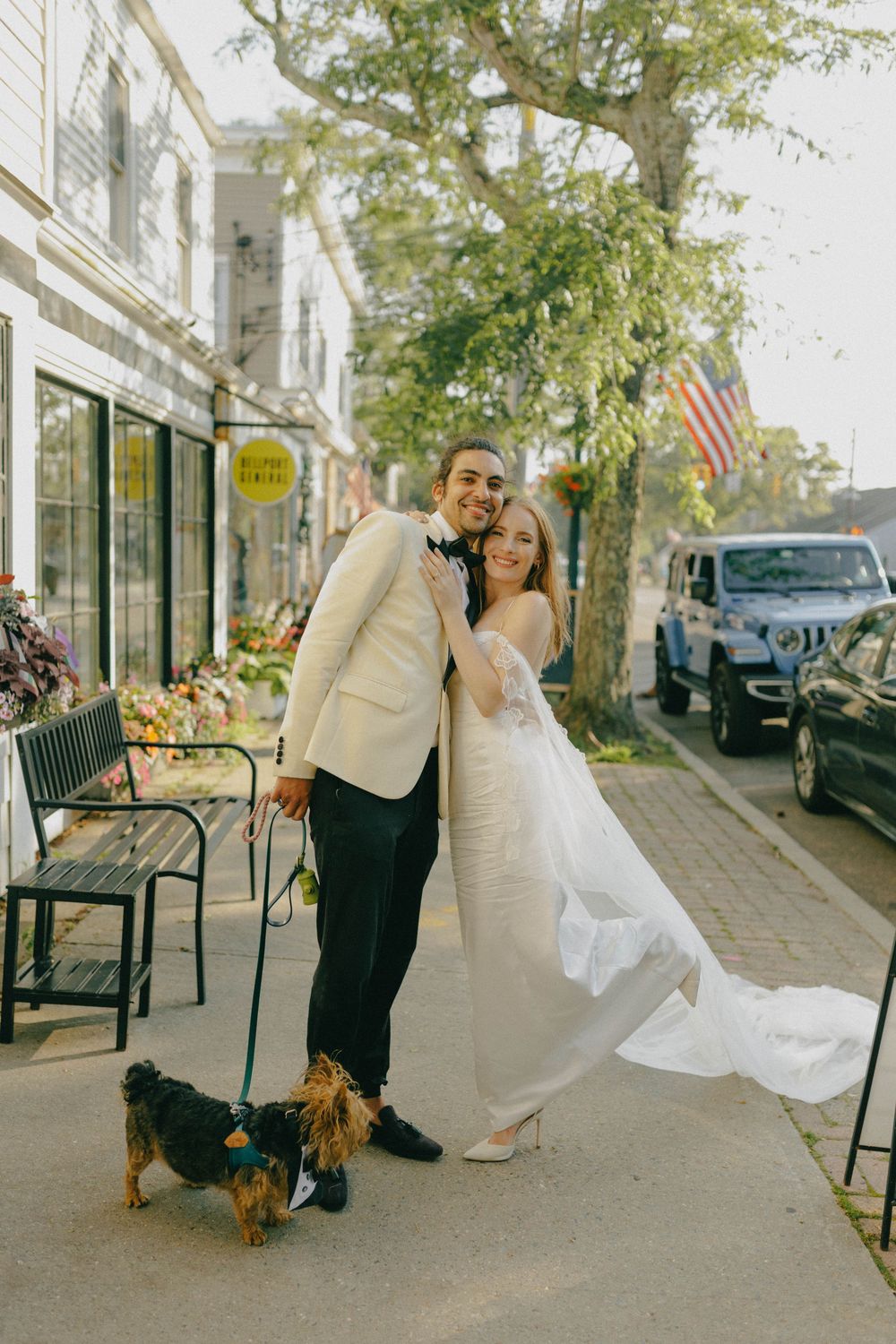 Bride and groom posing on a charming small-town street with their Yorkshire Terrier dog.