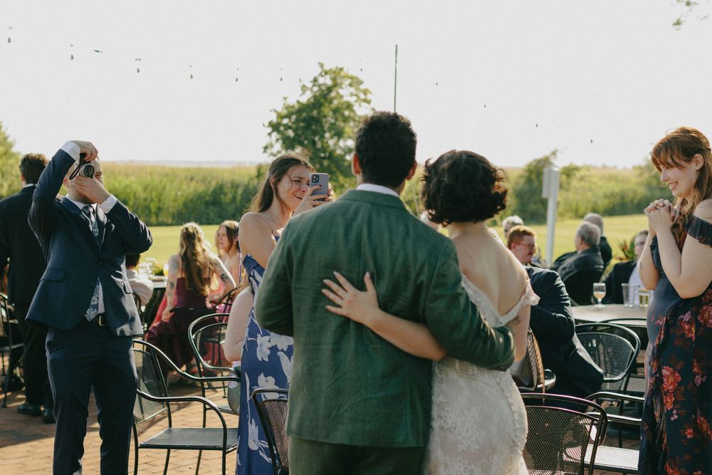 Newlyweds sharing first dance outdoors at golden hour with guests watching and celebrating.