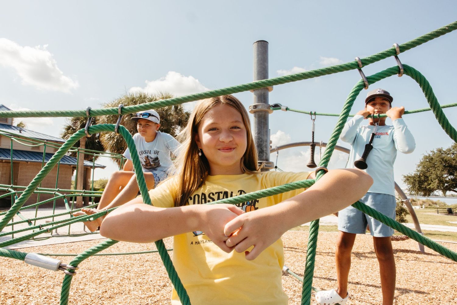 Children playing on a green rope climbing structure at an outdoor playground on a sunny day.