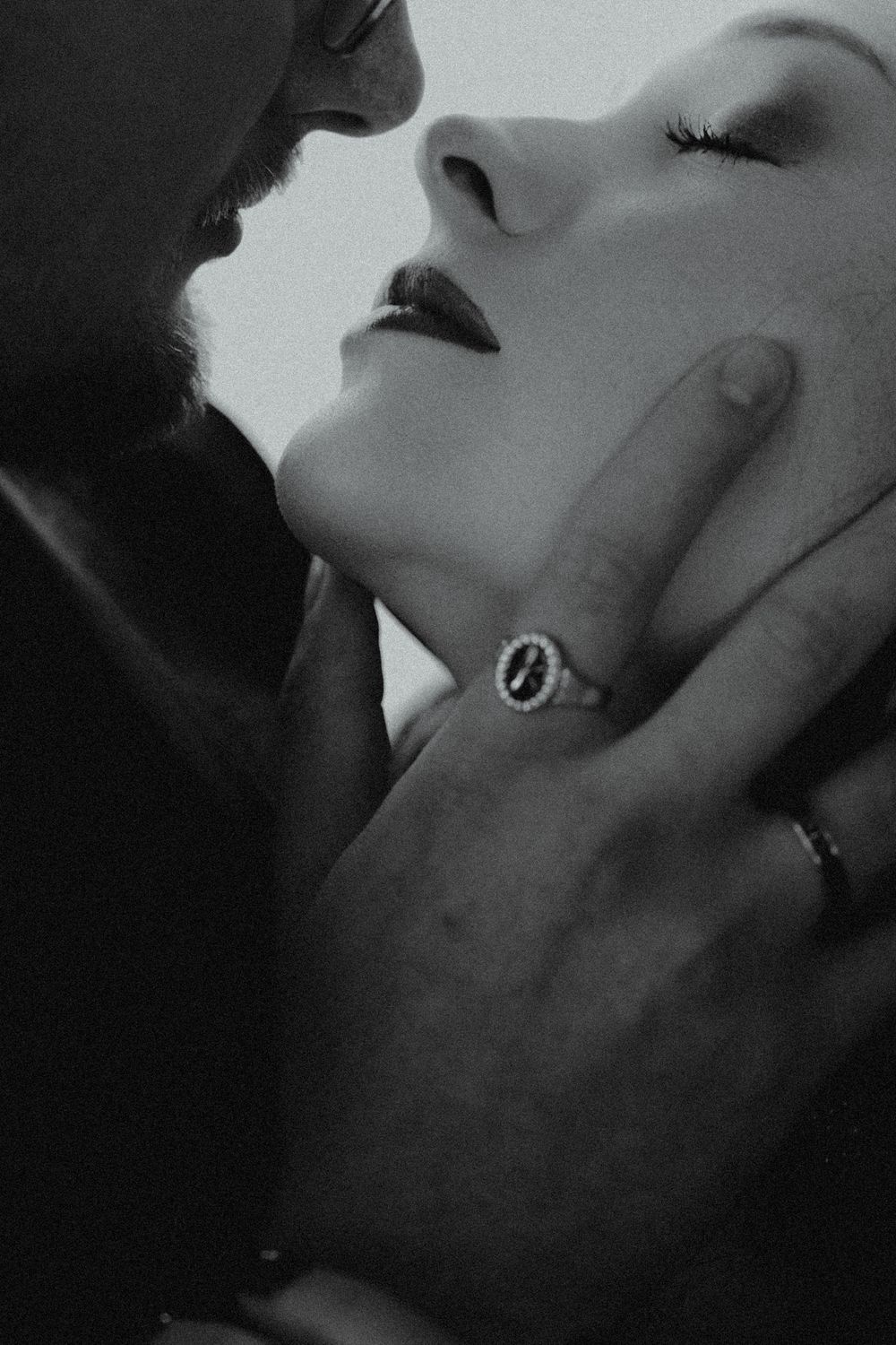 Black and white romantic photo of a couple almost kissing, man gently holding womans face, wearing elegant diamond ring.