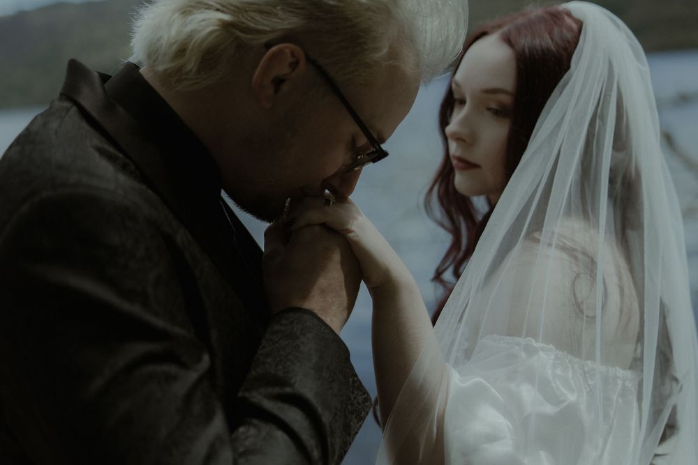 An elderly man with white hair kisses a young brides hand in a romantic wedding scene.