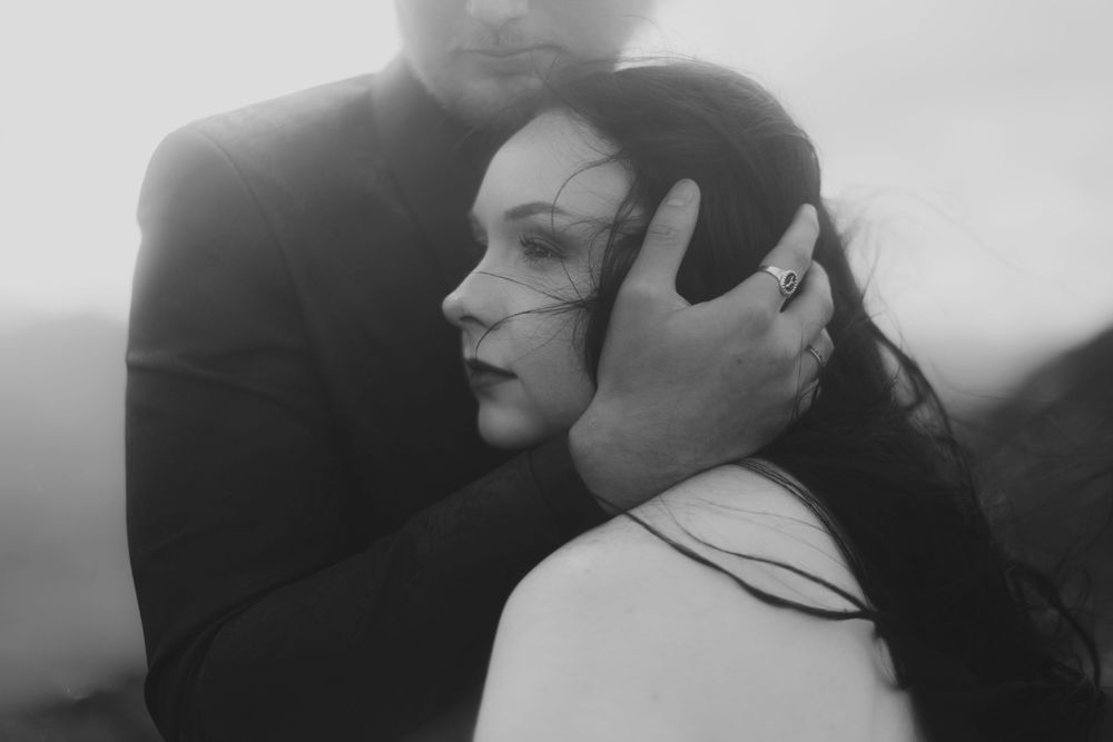 Black and white photo of a couple embracing romantically outdoors, man tenderly holding womans head against his chest.