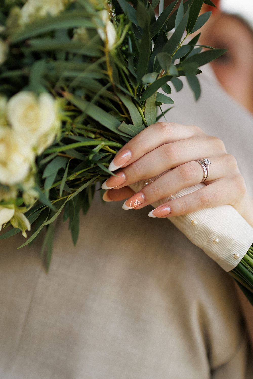Close-up of bride's hand with engagement ring holding white wedding bouquet.