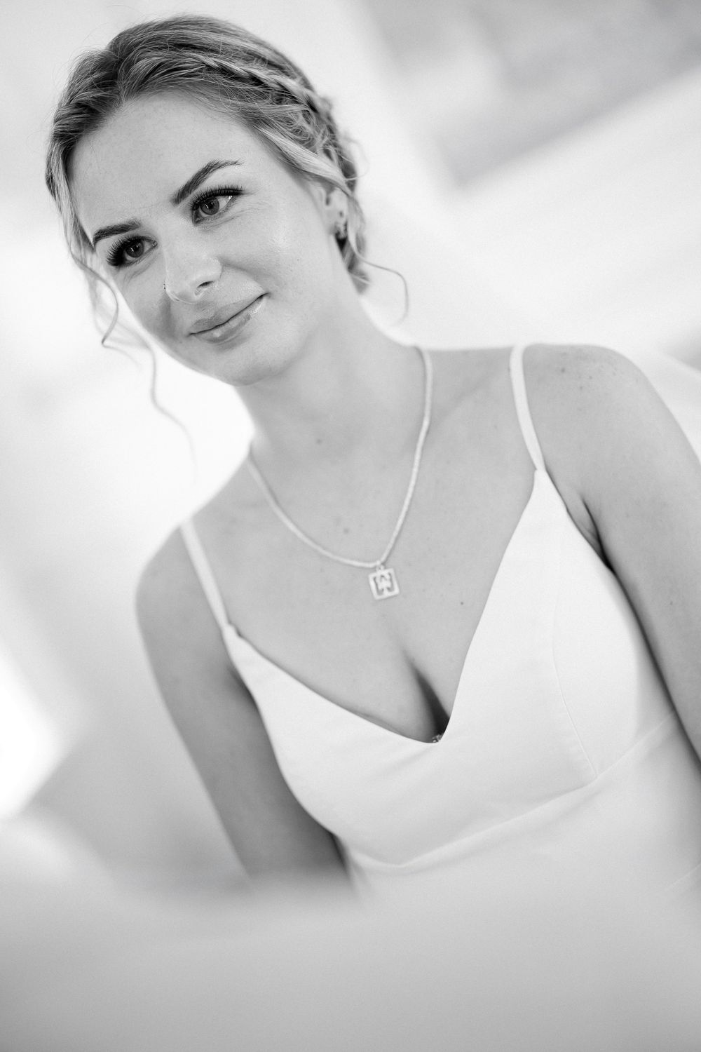 Elegant bride in white dress with pearl necklace and braided updo smiling softly in black and white portrait.