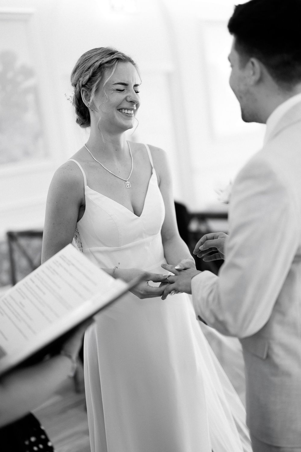 Bride smiling joyfully during ring exchange ceremony in elegant white gown.