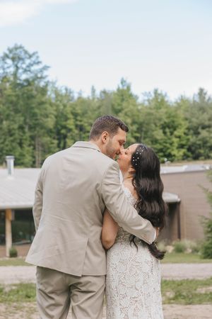 A bride and groom share a romantic kiss outdoors, surrounded by lush green trees on their wedding day.
