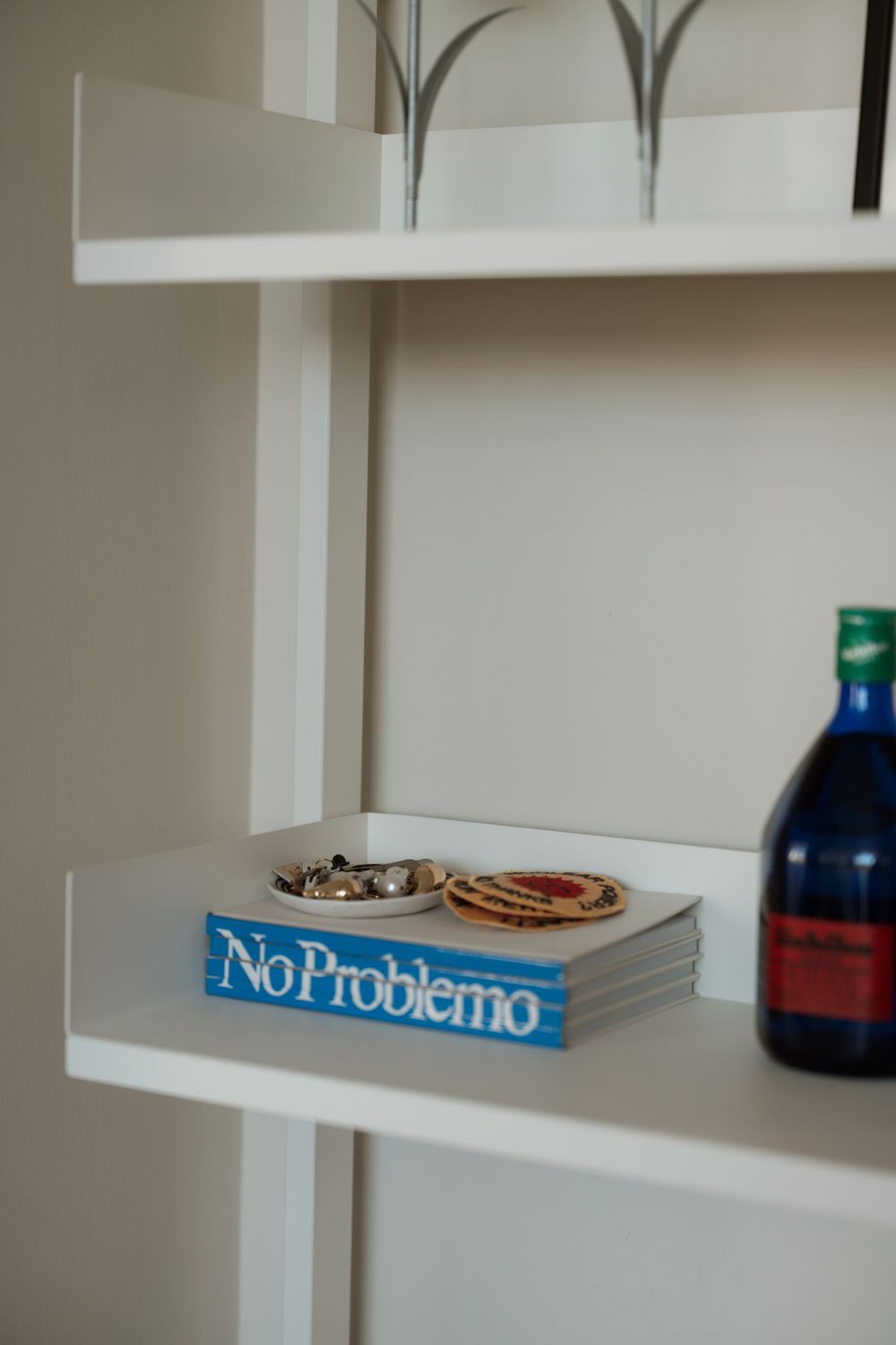 White shelving unit displaying a blue No Problemo book, decorative dishes, and a dark blue bottle.