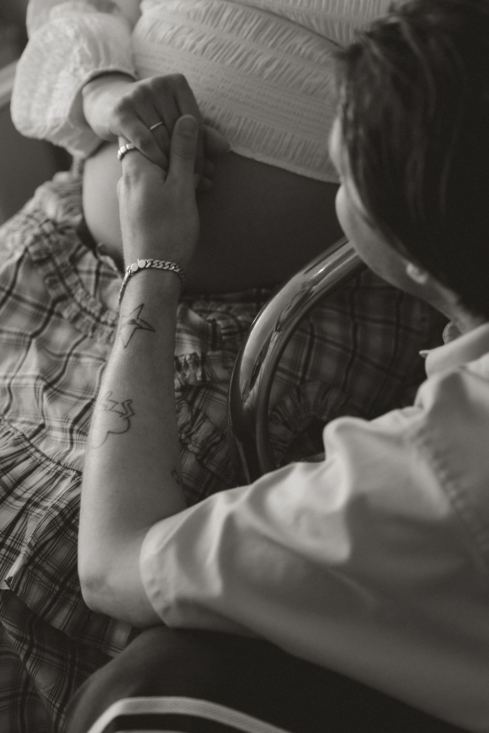 Black and white photo of a person with tattoos touching a pregnant woman's bare belly.