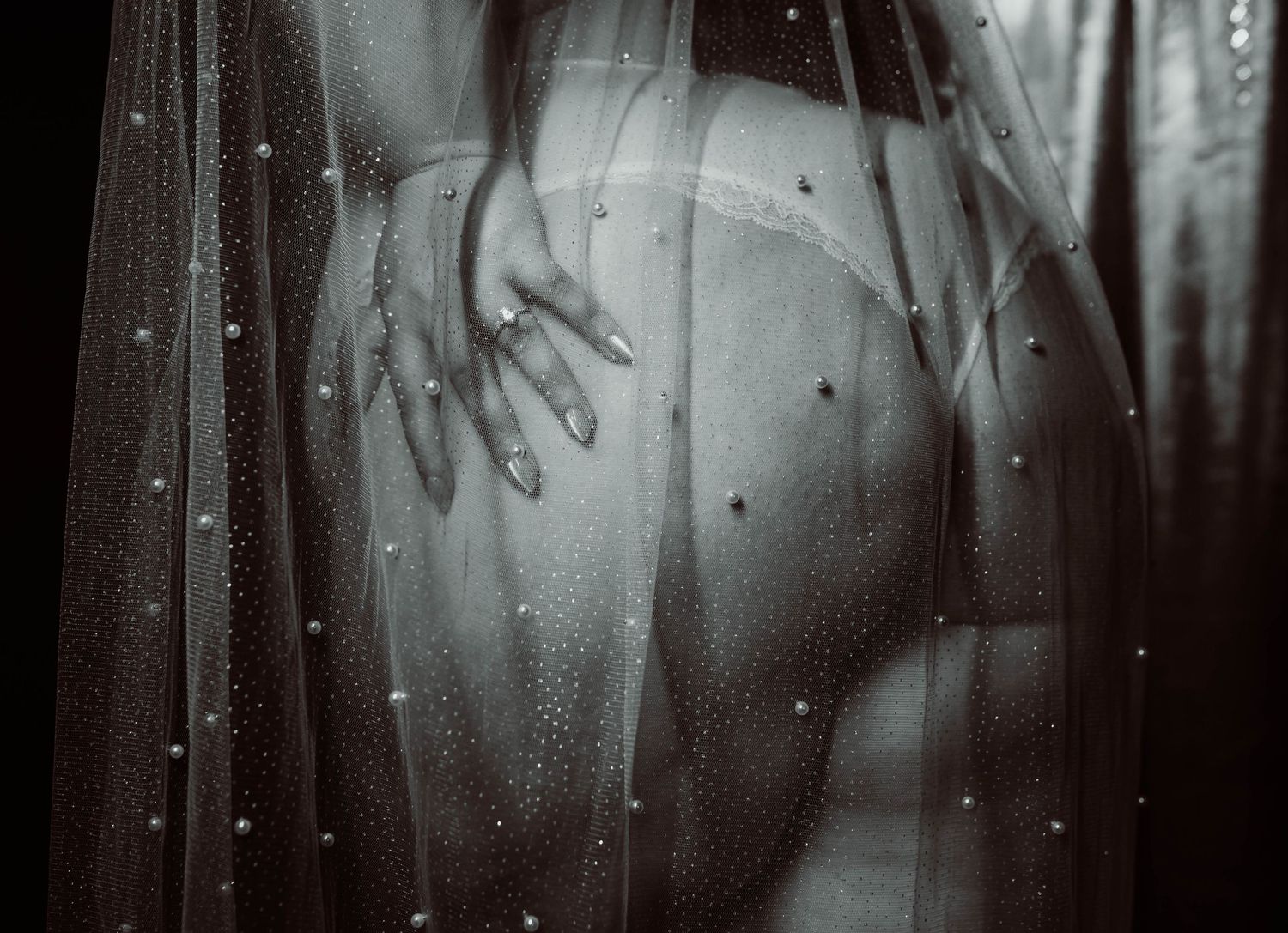 Artistic black and white boudoir photo of a woman draped in sheer embellished veil with pearl details for her bridal boudoir photoshoot.