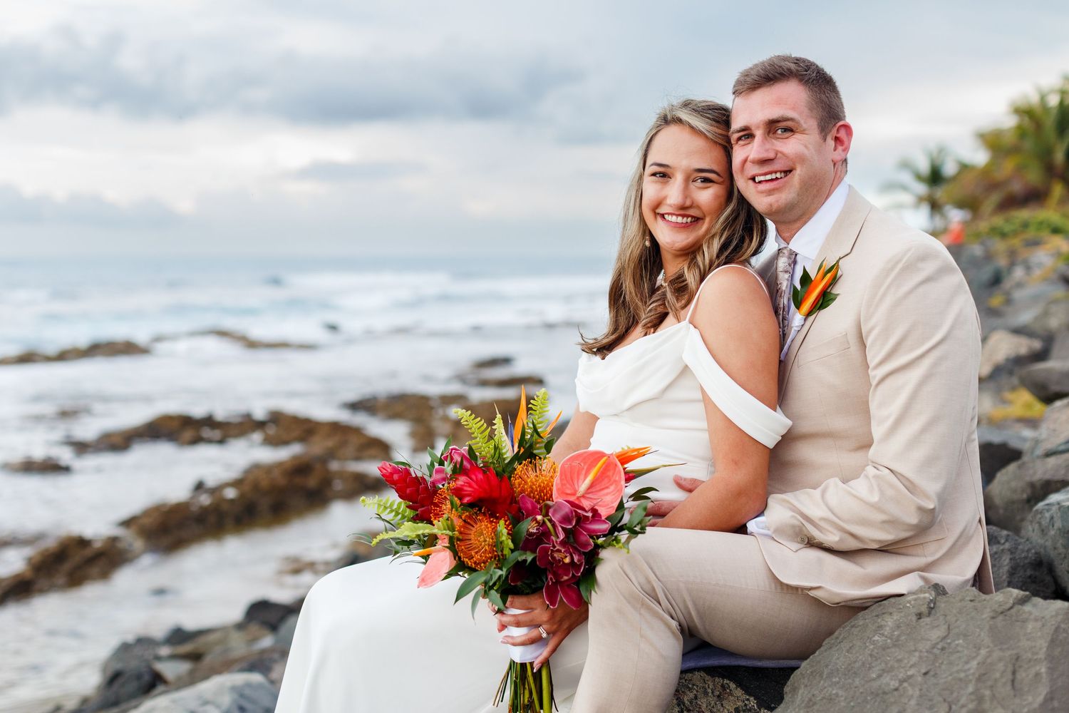 Wedding portrait. Bride and groom sitting on rocks at the water's edge at the beach. Balneario del Escambrón, Old San Juan, Puerto Rico.