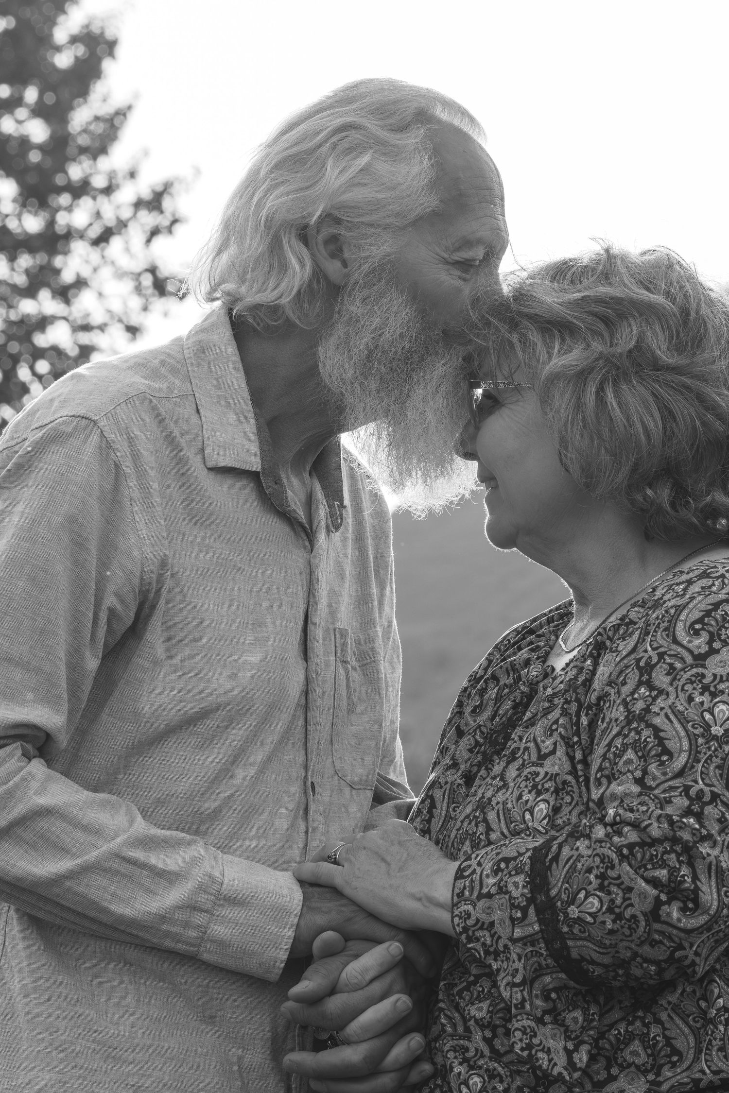 Black and white photo of an elderly couple sharing a tender kiss while holding hands outdoors.