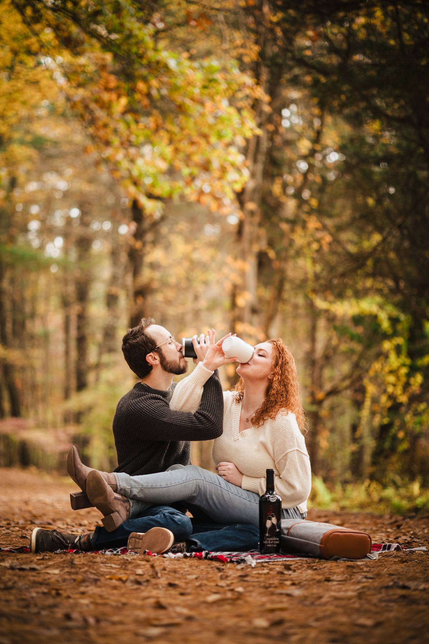 Engaged couple sitting together on a picnic blanket at Borderland State Park, drinking together from tumblers, legs tangled together