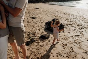 Father and toddler playing on a sandy beach at golden hour, child reaching up with arms raised.