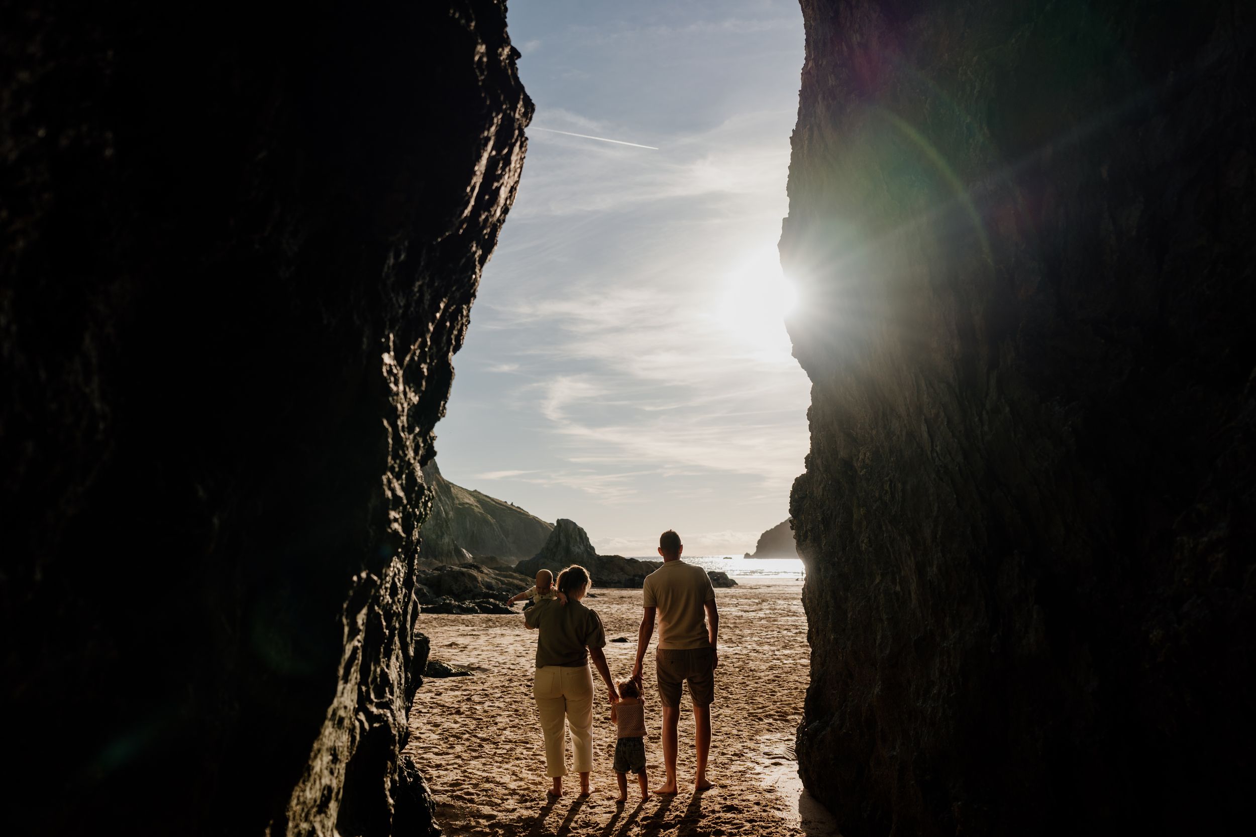 Silhouette of family holding hands on sandy beach framed by dramatic rock formations with sunlight streaming through.