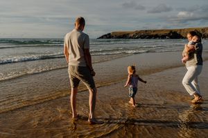Family of four enjoying a peaceful beach walk at sunset, with two young children playing near the ocean waves.